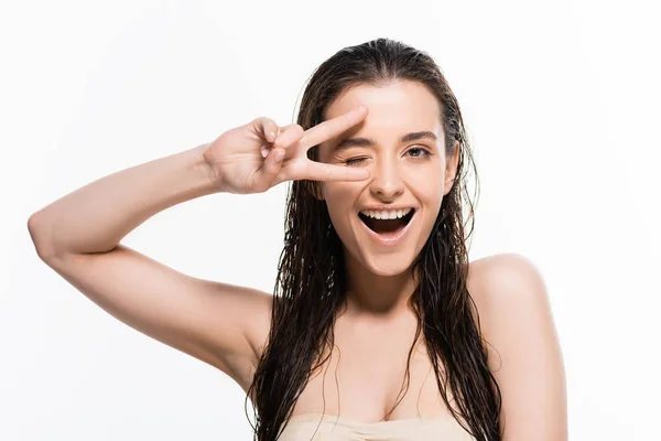 Hermosa mujer joven mojada guiñando el ojo y mostrando signo de paz aislado en blanco - foto de stock