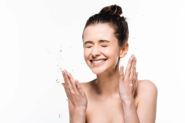 Feliz mujer morena joven desnuda con belleza natural y ojos cerrados lavándose con agua limpia salpicadura aislada en blanco - foto de stock
