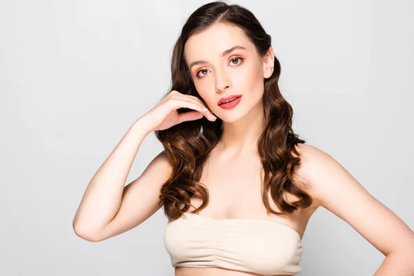 Beautiful brunette woman with curls and makeup touching face isolated on grey — Stock Photo