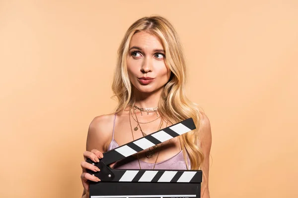 Блондинка у фіолетовій атласному платті з дошкою для фільмів, що дивиться далеко на бежевий фон — стокове фото