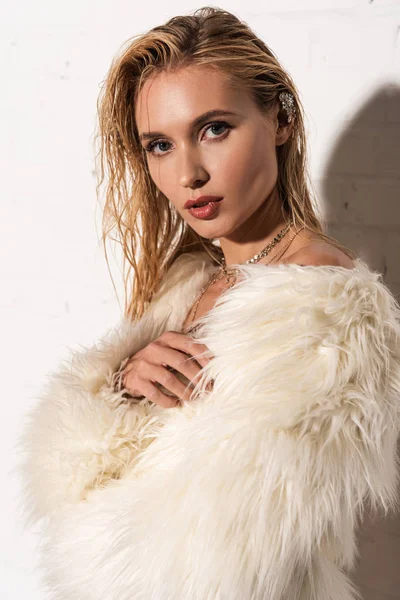 Sexy young woman with wet hair in white faux fur coat on white background — Stock Photo