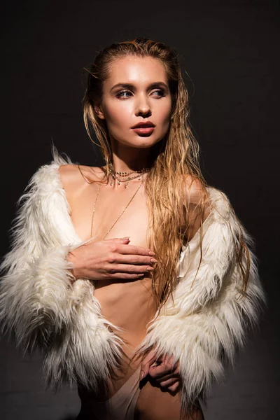 Sexy naked young woman with wet blonde hair and hand on breast in white faux fur coat and looking away isolated on black — Stock Photo