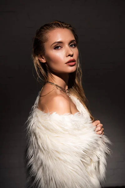 Side view of sexy naked young woman with wet blonde hair in white faux fur coat isolated on black — Stock Photo