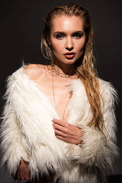 Sexy naked young woman with wet blonde hair in white faux fur coat looking at camera isolated on black — Stock Photo