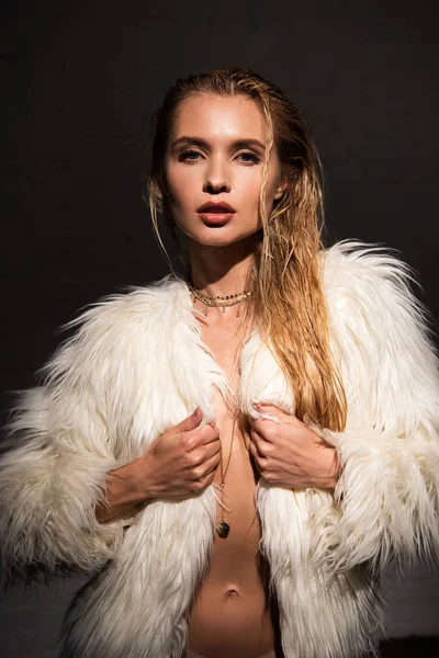 Sexy naked young woman with wet blonde hair in faux fur coat isolated on black — Stock Photo