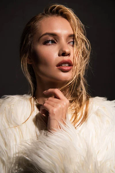 Sexy young woman with wet blonde hair in white faux fur coat isolated on black — Stock Photo