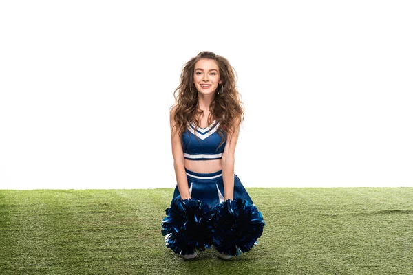 Sexy felice cheerleader ragazza in uniforme blu seduta con pompon su campo verde isolato su bianco — Foto stock