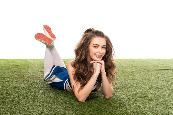 Happy cheerleader girl in blue uniform lying on green field isolated on white — Stock Photo