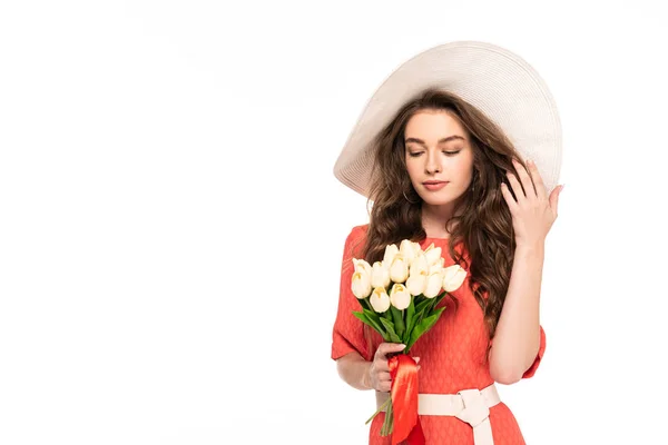 Mujer elegante en sombrero y vestido mirando tulipanes blancos aislados en blanco - foto de stock