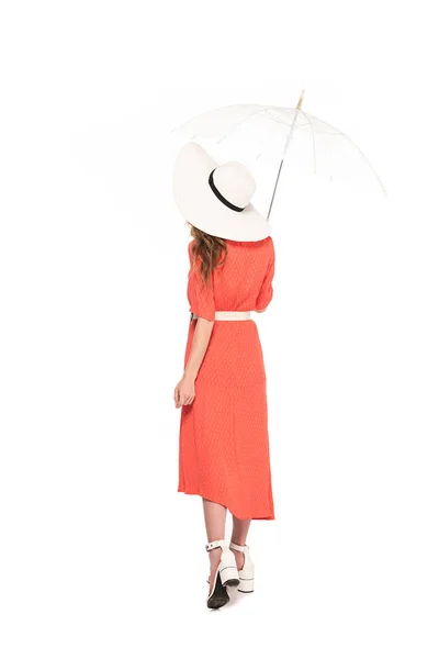 Back view of elegant woman in hat and dress holding transparent umbrella isolated on white — Stock Photo
