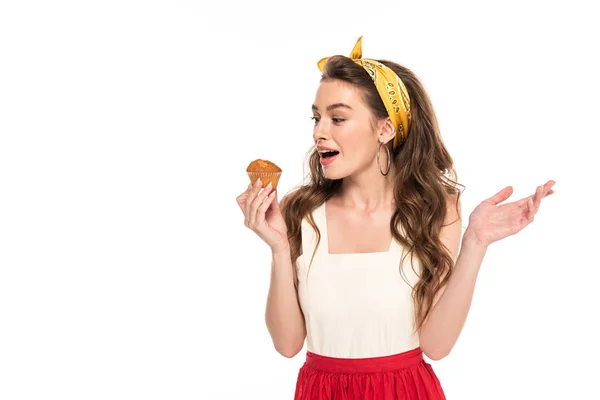 Young excited housewife in dress and apron looking at muffin isolated on white — Stock Photo