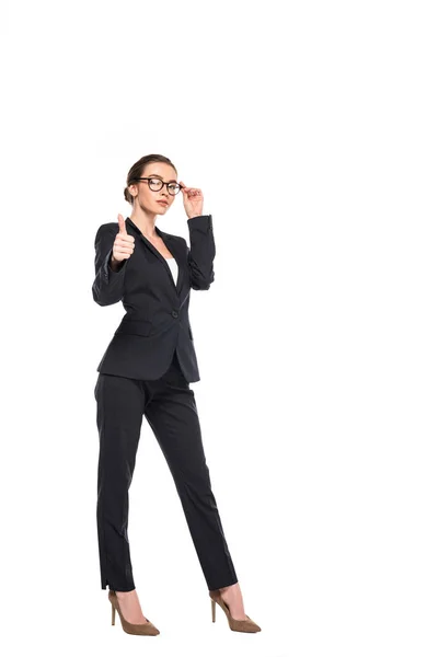 Повний вигляд молодої успішної бізнес-леді в чорному костюмі і окулярах, що показують великий палець вгору ізольовано на білому — стокове фото