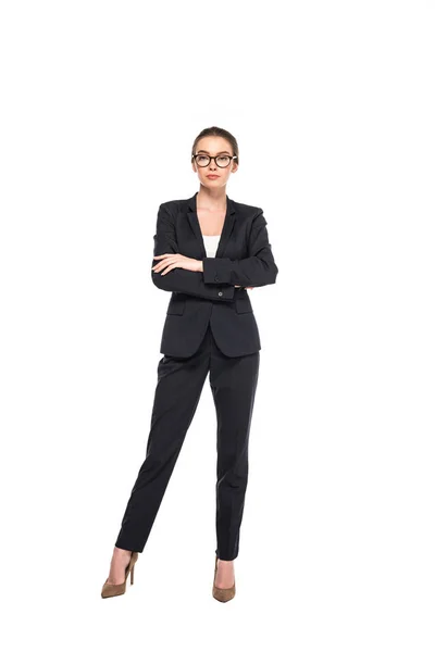 Vista completa de la joven empresaria de éxito en traje negro y gafas con brazos cruzados aislados en blanco - foto de stock