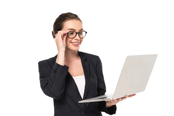 Молода усміхнена бізнес-леді в чорному костюмі і окулярах тримає ноутбук ізольовано на білому — стокове фото