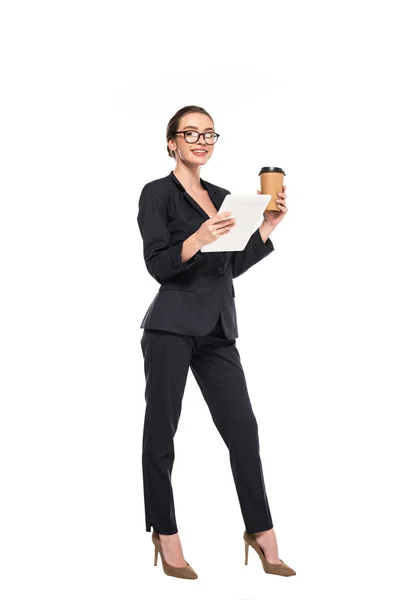 Joven empresaria sonriente en traje negro y gafas sosteniendo café para llevar y tableta digital aislada en blanco - foto de stock