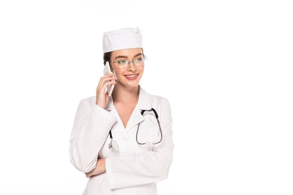 Молодий щасливий лікар у білому пальто зі стетоскопом розмовляє на смартфоні ізольовано на білому — стокове фото