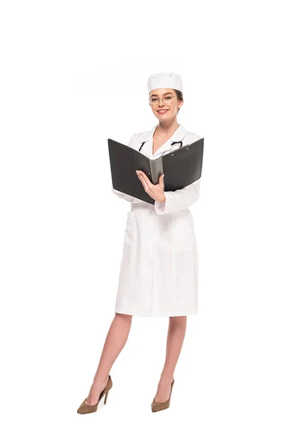 Ganzkörperansicht des jungen lächelnden Arztes in weißem Mantel mit Stethoskop und Ordner isoliert auf weiß — Stockfoto