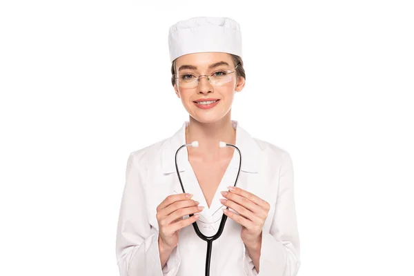 Молодой улыбающийся доктор в белом халате, держащий стетоскоп изолированным на белом — стоковое фото