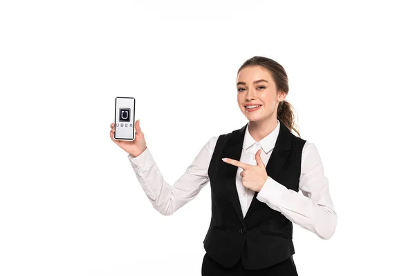 KYIV, UKRAINE - 7 AVRIL 2019 : heureuse jeune serveuse pointant du doigt l'application uber sur smartphone isolé sur blanc — Photo de stock