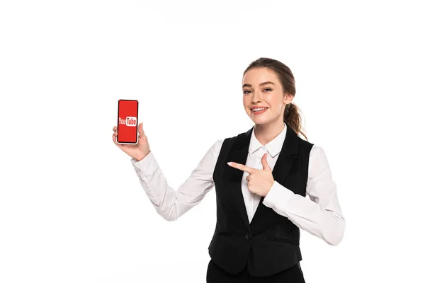 KYIV, UCRANIA - 7 DE ABRIL DE 2019: joven camarera feliz señalando con el dedo la aplicación de youtube en un teléfono inteligente aislado en blanco - foto de stock