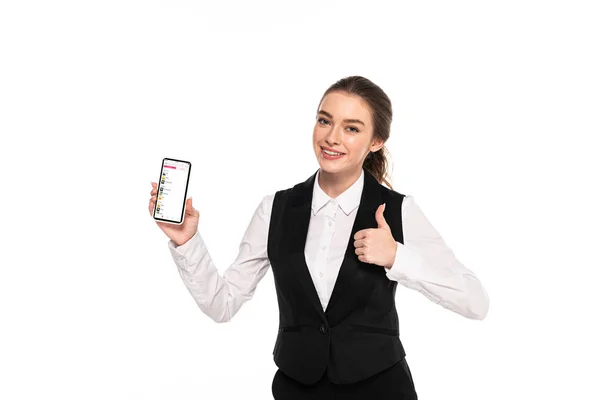 KYIV, UCRANIA - 7 DE ABRIL DE 2019: joven camarera feliz sosteniendo teléfono inteligente con aplicación de música de manzana y mostrando el pulgar hacia arriba aislado en blanco - foto de stock