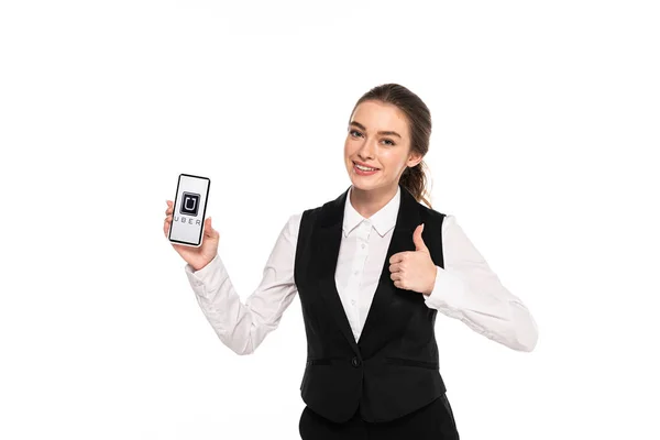 КИЕВ, УКРАИНА - 7 апреля 2019 года: счастливая молодая официантка держит смартфон с приложением Uber и показывает большой палец, изолированный на белом — стоковое фото