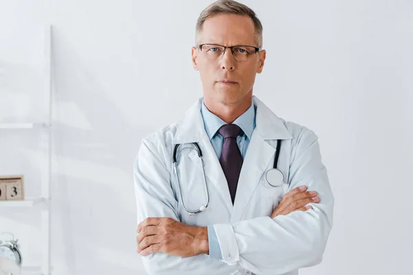 Arzt mit Stethoskop steht mit verschränkten Armen und blickt in Kamera — Stockfoto