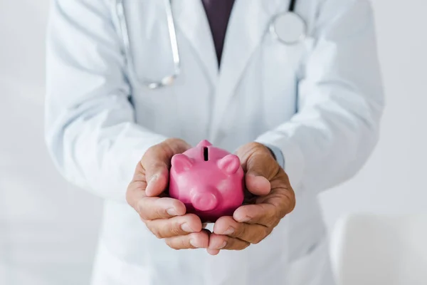 Abgeschnittene Ansicht eines Mannes im weißen Mantel, der ein rosafarbenes Sparschwein in den Händen hält — Stockfoto