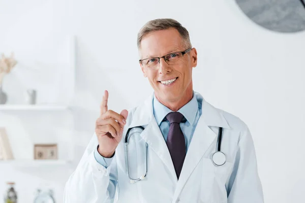 Cheerful doctor smiling while pointing with finger while looking at camera — Stock Photo