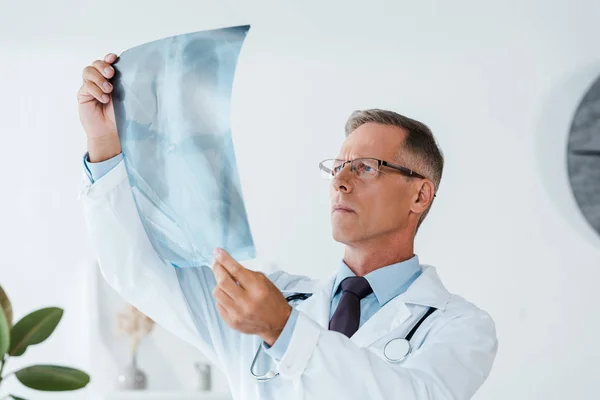 Médico grave em casaco branco e óculos segurando raio-X no hospital — Fotografia de Stock