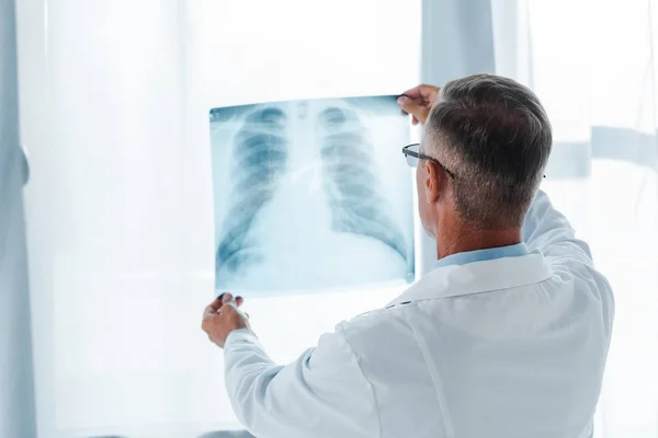 Vista posterior del médico de bata blanca sosteniendo rayos X en el hospital - foto de stock