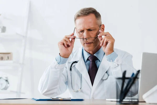 Selektiver Fokus eines gutaussehenden Arztes, der Brille im Krankenhaus anfasst — Stockfoto