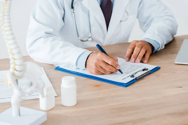 Cropped view of doctor with stethoscope writing diagnosis in hospital — Stock Photo