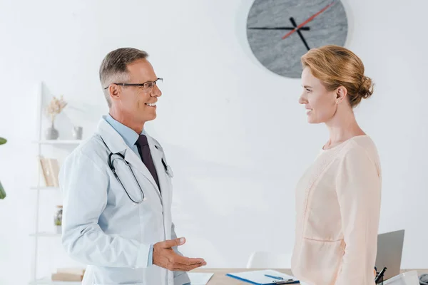 Cheerful doctor gesturing while looking at attractive woman — Stock Photo