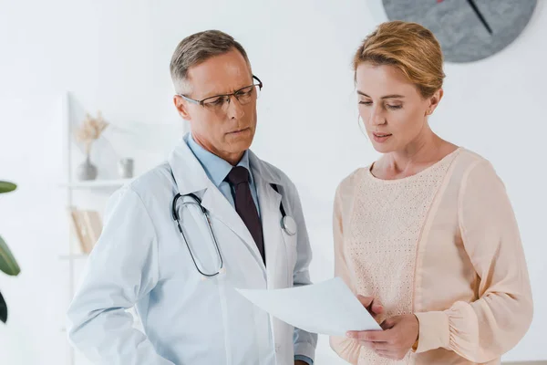 Handsome doctor in glasses and woman looking at document — Stock Photo