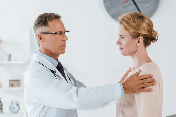 Médecin dans les lunettes toucher femme tout en examinant à la clinique — Photo de stock