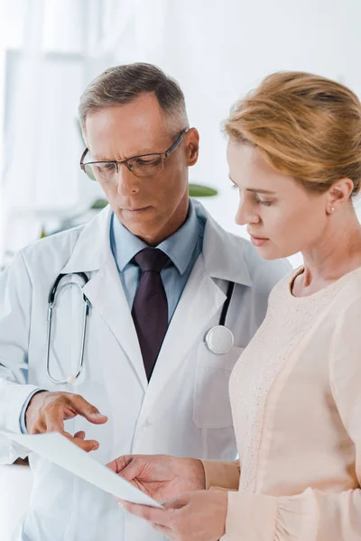 Arzt in Brille zeigt mit Finger auf Dokument in der Nähe von Frau — Stockfoto