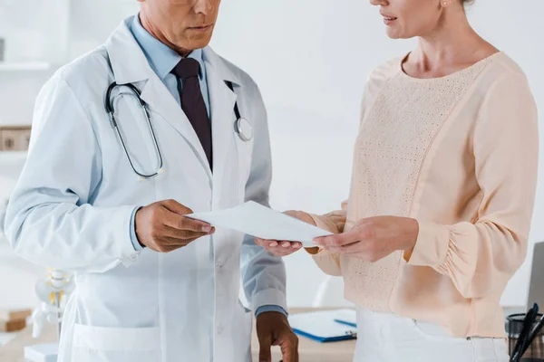 Cropped view of doctor and woman holding document in clinic — Stock Photo