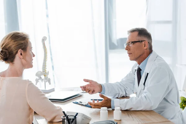 Arzt mit Brille schaut Frau an, während sie am Tisch sitzt — Stockfoto