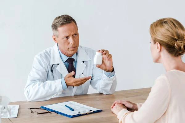 Enfoque selectivo del médico en bata blanca mirando a la mujer y el gesto mientras sostiene la botella en el hospital — Stock Photo