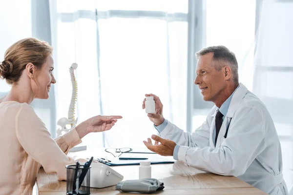 Attractive woman pointing with finger at bottle near happy doctor — Stock Photo