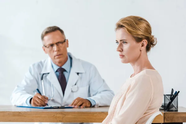 Enfoque selectivo de la mujer molesta sentada cerca del médico en bata blanca - foto de stock