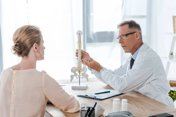 Selective focus of doctor in glasses touching spine model near patient — Stock Photo