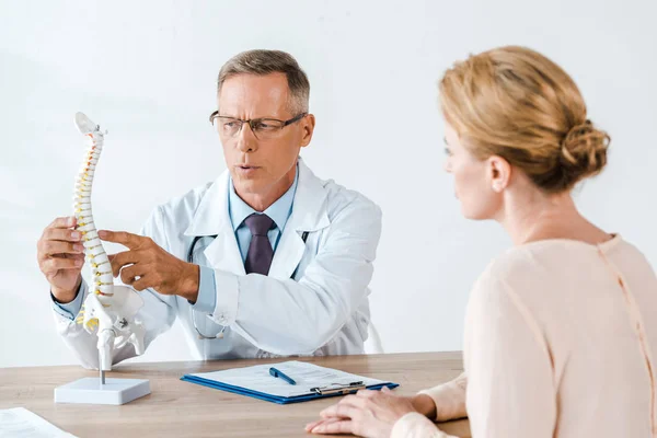 Selective focus of doctor in glasses touching spine model near woman — Stock Photo