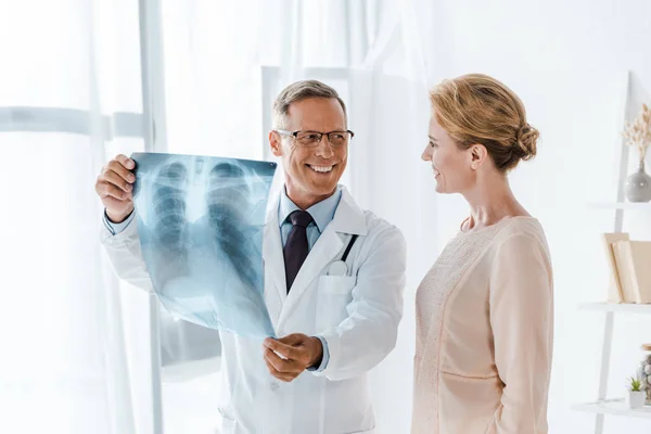 Médecin heureux regardant patient attrayant et tenant des rayons X dans la clinique — Photo de stock