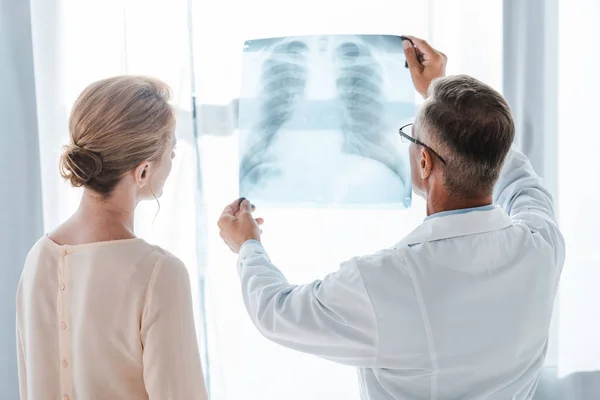 Médecin en manteau blanc et femme regardant la radiographie à la clinique — Photo de stock
