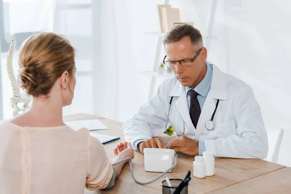 Selective focus of doctor in glasses measuring blood pressure of woman — Stock Photo