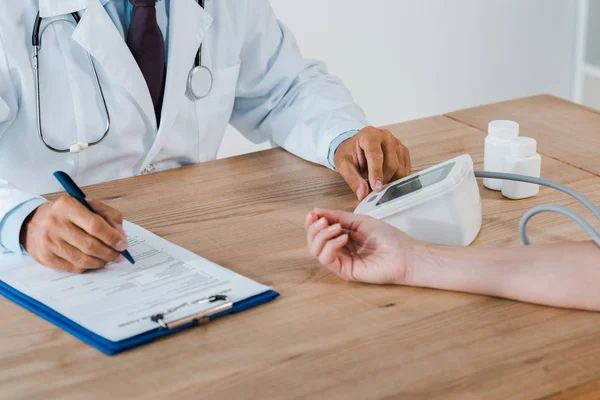 Vista recortada del médico sosteniendo la pluma cerca del portapapeles mientras mide la presión arterial de la mujer - foto de stock