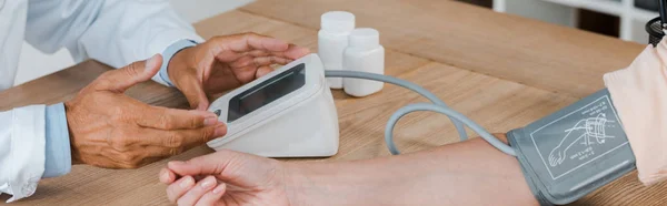 Panoramic shot of doctor gesturing while measuring blood pressure of woman — Stock Photo