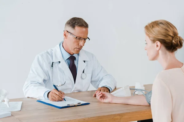 Médico guapo medir la presión arterial de la mujer atractiva en la clínica - foto de stock